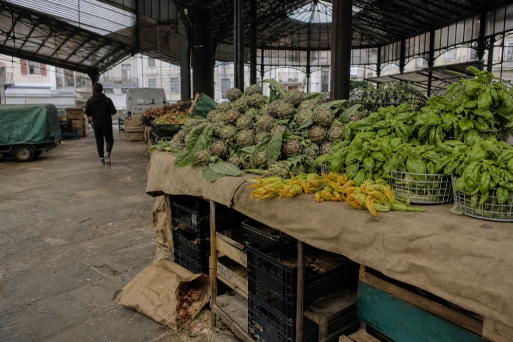 A market stall piled with fresh vegetables and baskets of herbs