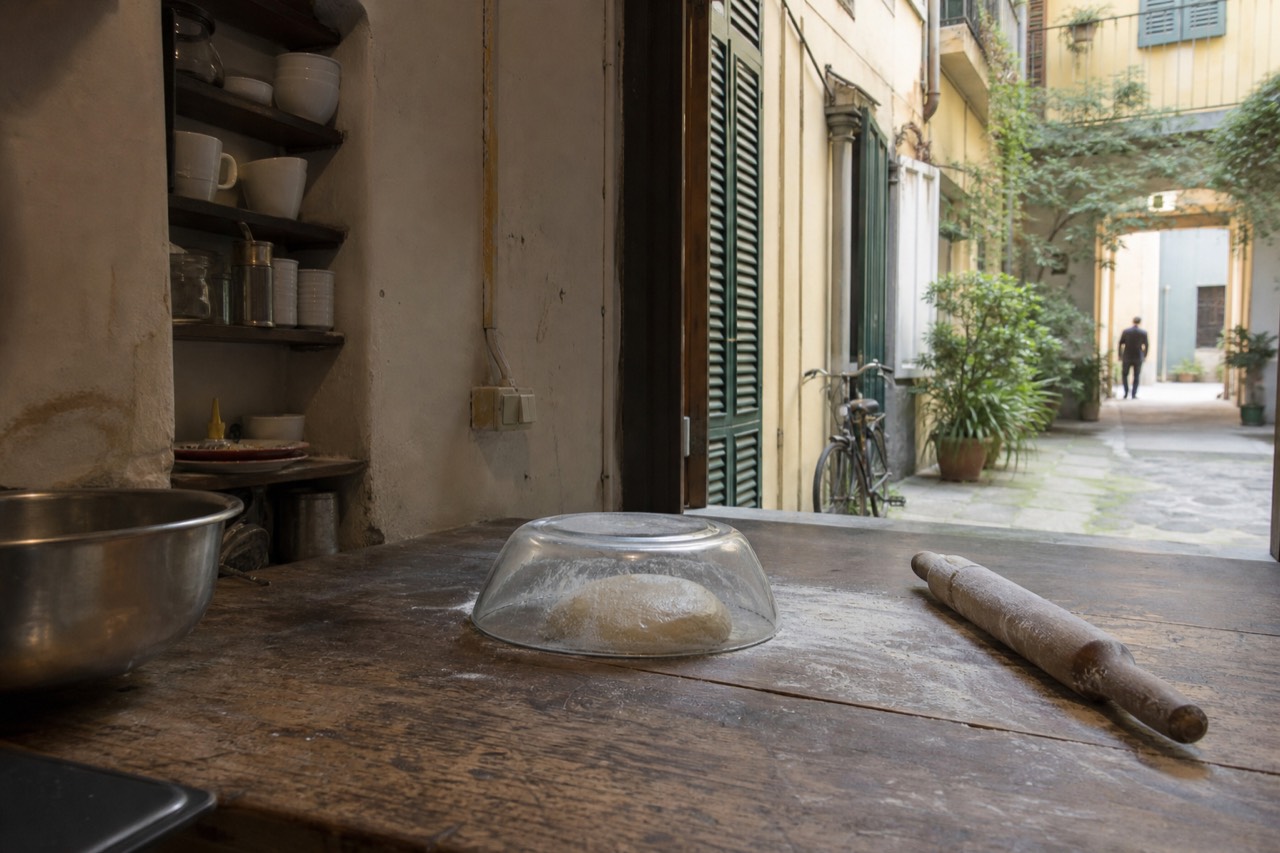 A rustic kitchen counter with fresh pasta dough, a rolling pin and flour