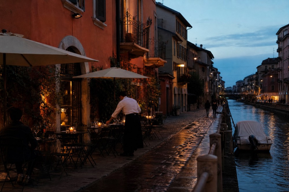 Outdoor tables lining a narrow Naviglio Grande lane with red-orange buildings above