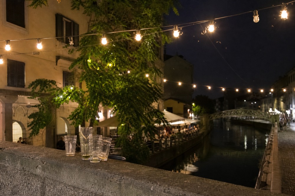 String lights strung above the Navigli towpath in Milan on a warm summer night, terraces crowded along the water