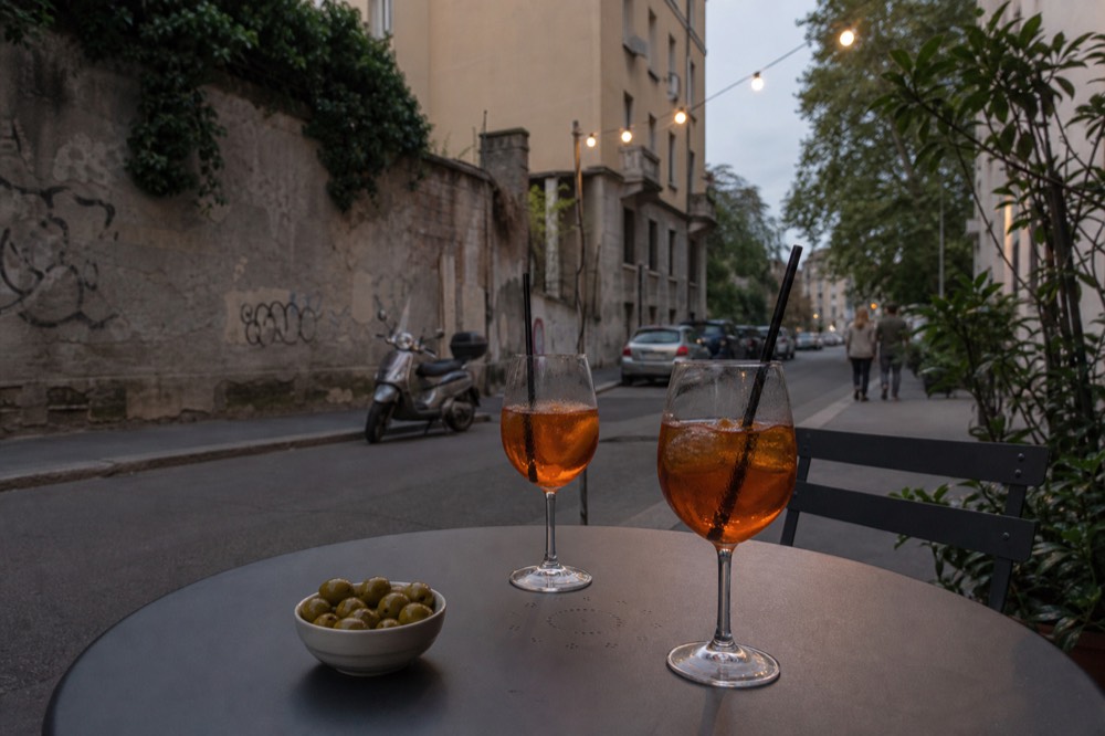 A spritz and a bowl of olives on a round metal table on a Milan side street on a cool spring evening
