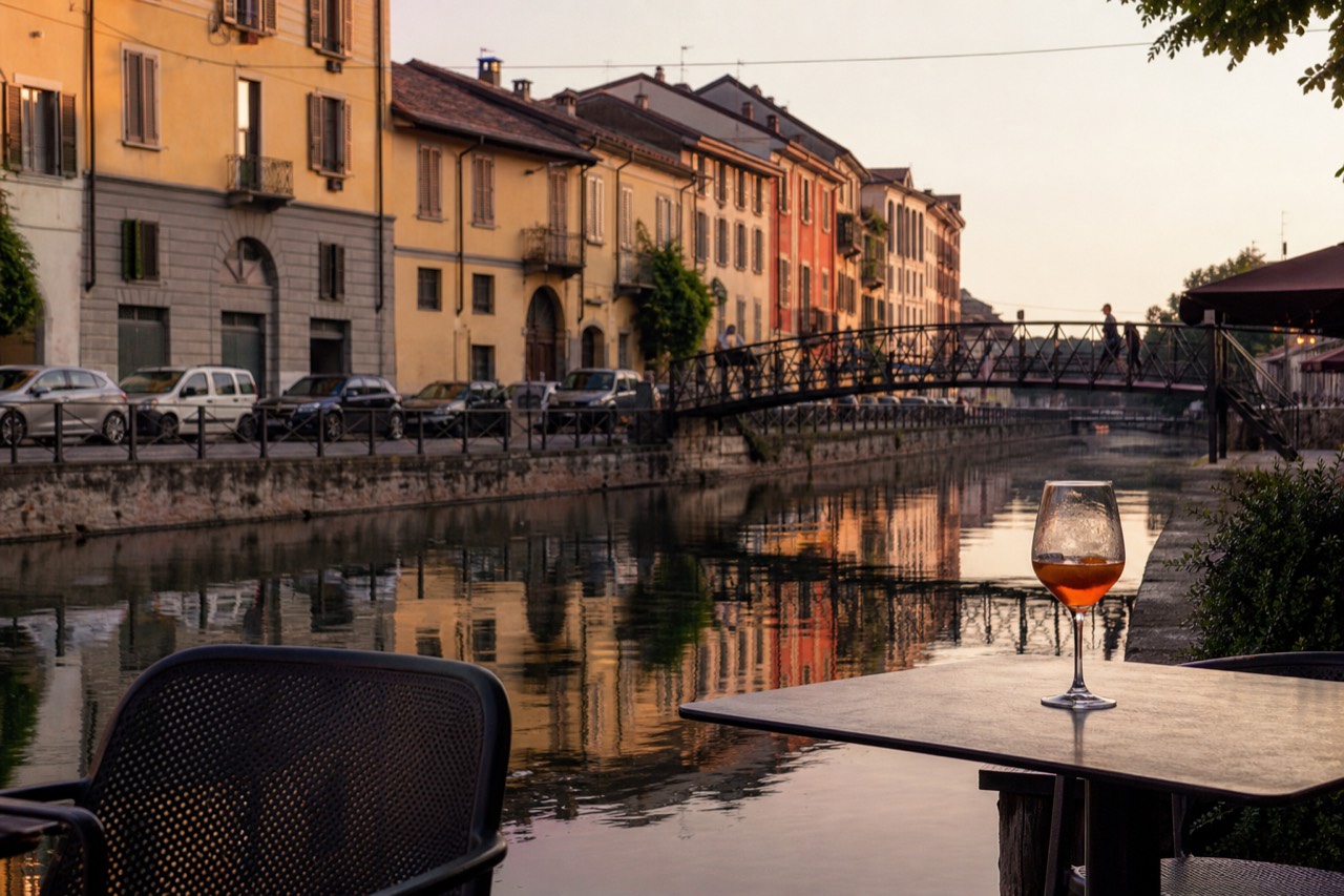 Dusk on a Naviglio Grande café terrace with the basin and iron footbridge behind