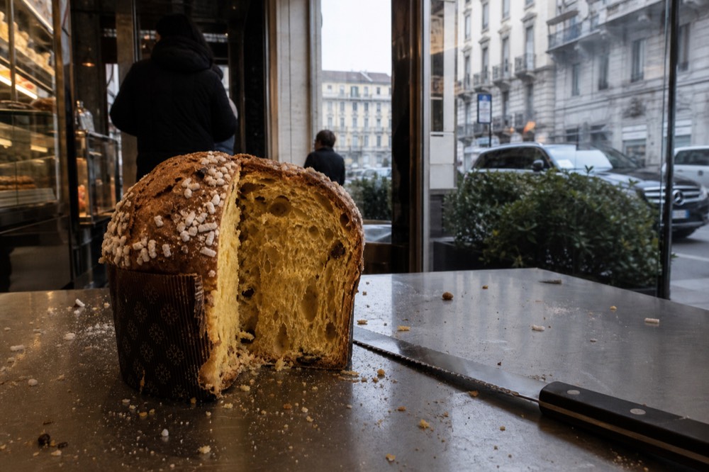 Hands slicing a tall wedge from a domed panettone loaf with a long serrated knife