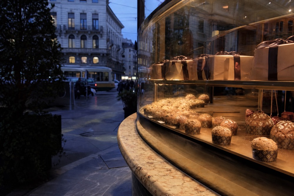 A pastry counter in Milan displaying small individual panettone loaves and wrapped sweet boxes