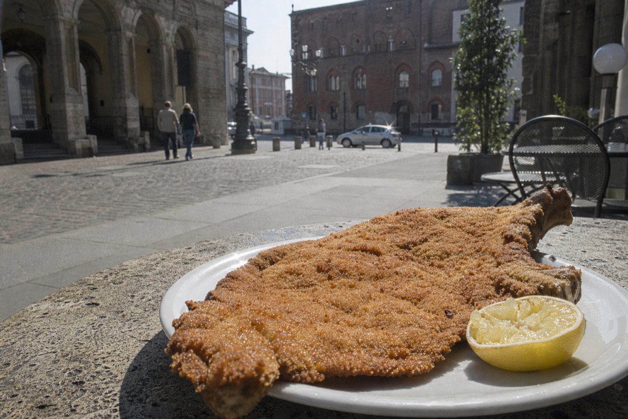 A golden bone-in breaded veal cutlet with a squeezed lemon half, on a stone table in Milan's Piazza dei Mercanti