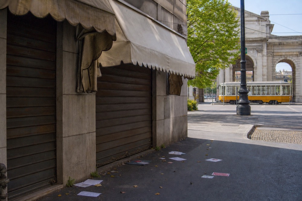 A shuttered restaurant storefront with a faded awning on a quiet Milan street in daytime