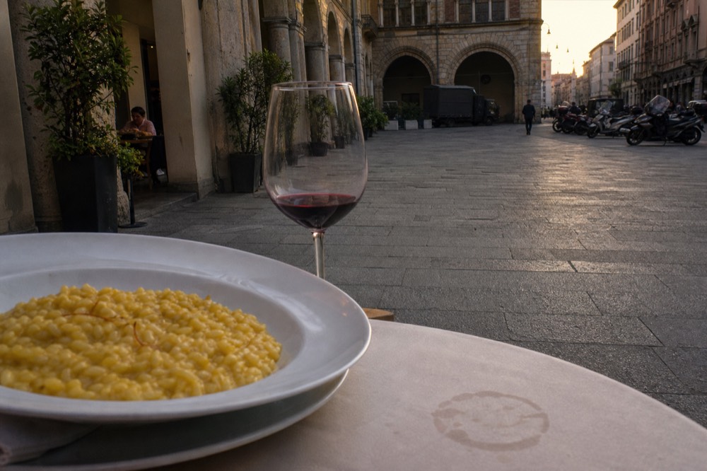 A bowl of saffron risotto and a half-drunk glass of red wine on a restaurant table in medieval Milan