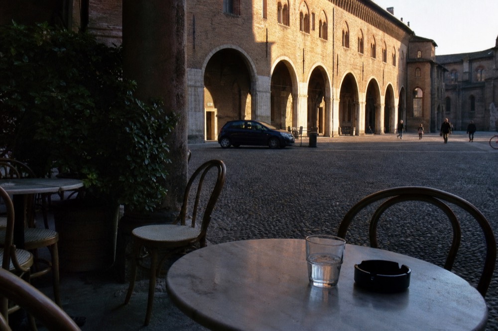 A Milan cafe terrace with small marble tables and chairs facing a historic street