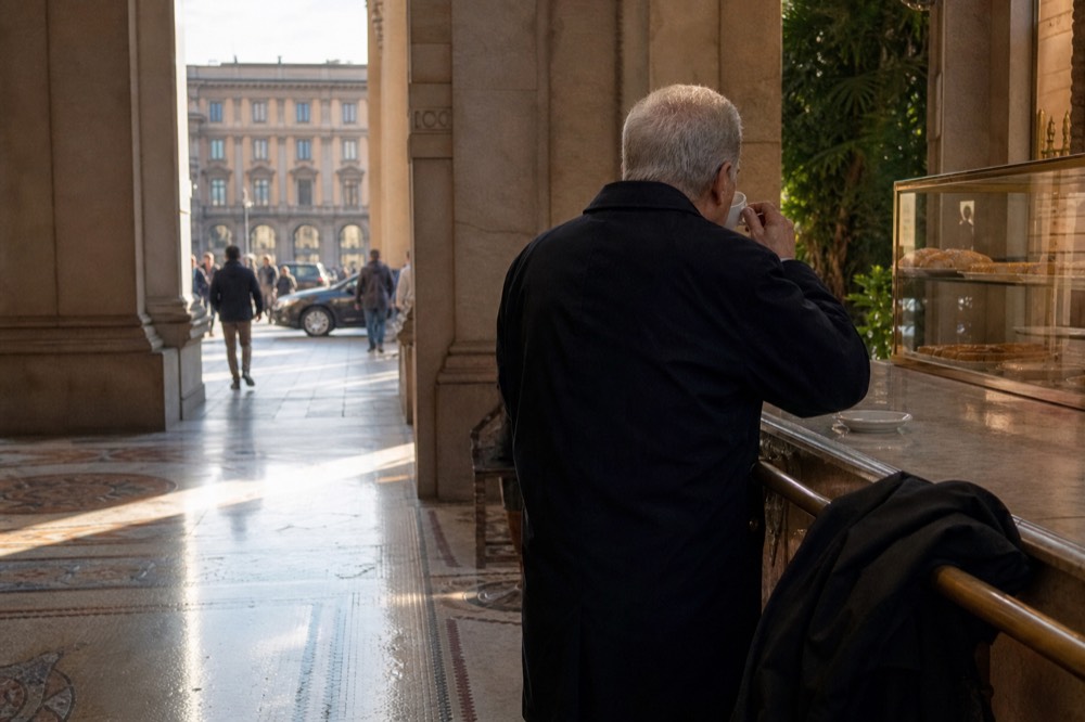 A customer standing at a marble bar counter drinking espresso in a Milan cafe
