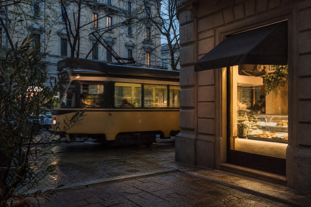 A Milan tram passing a pastry shop window at dusk