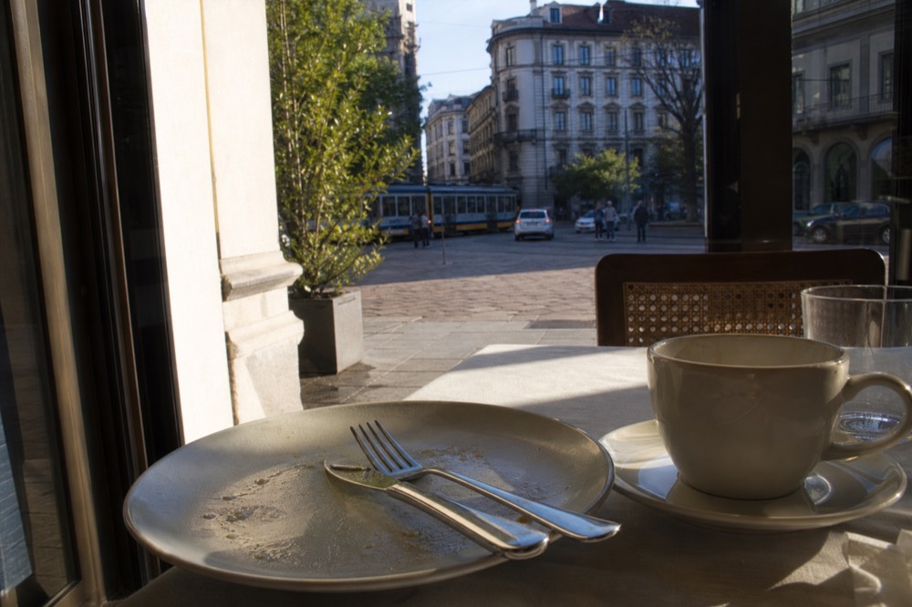 Cutlery resting parallel on a finished restaurant plate beside a coffee cup