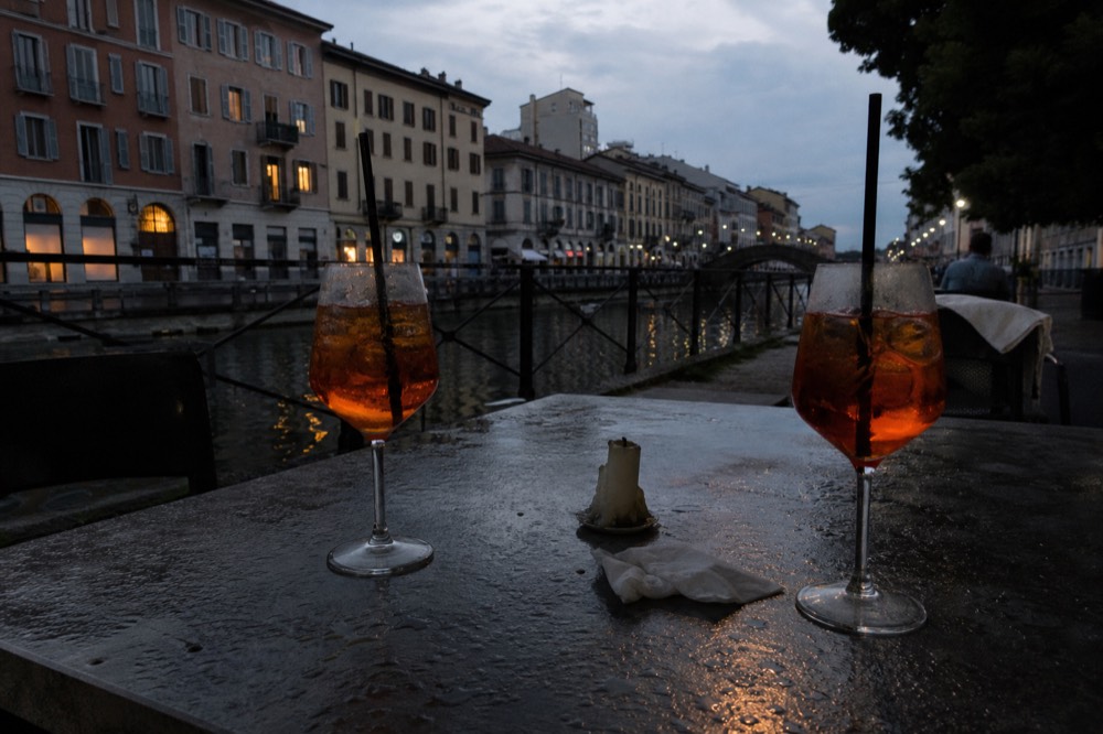A bright orange spritz and Campari-based aperitivo drinks on a canal-side table in Milan
