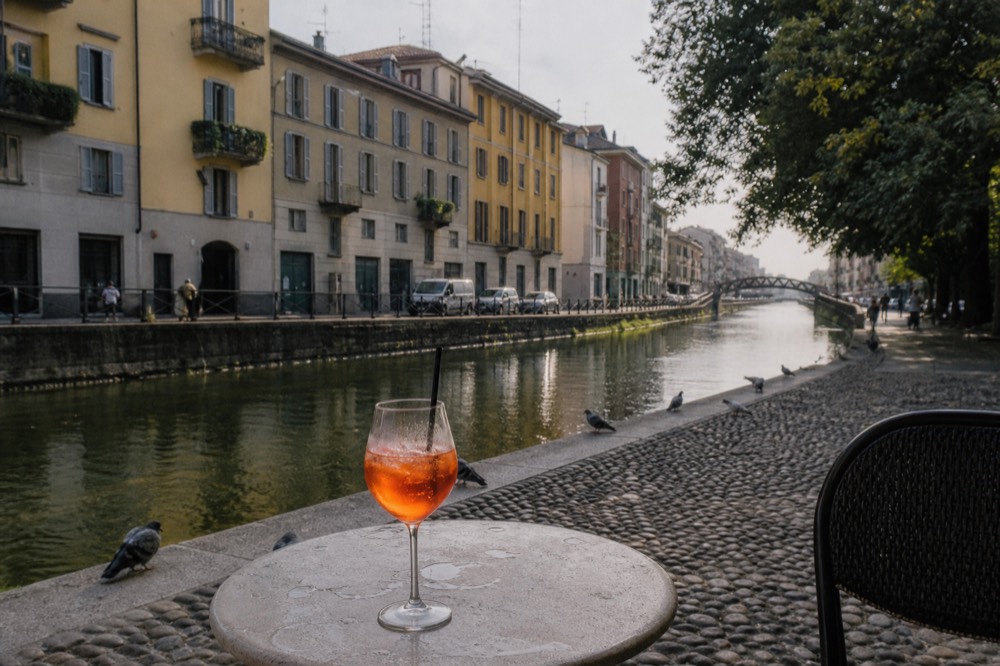 A glass of Aperol Spritz on a small table with Milanese canal light in the background