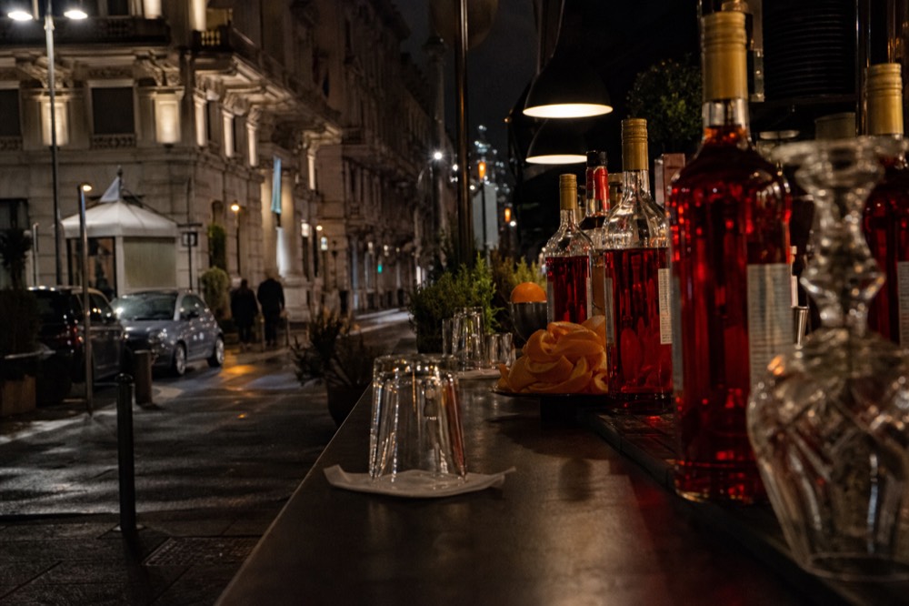 A dark bar counter with Campari bottles and orange peel garnishes under low light in Milan