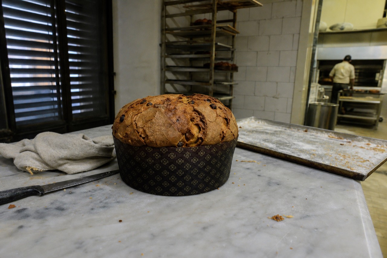 A whole panettone with its cracked top crust on a marble counter beside a knife and a linen cloth