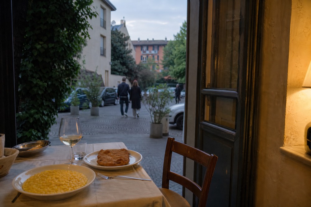 A table set with a plate of saffron risotto, a cutlet and a glass of white wine in a Milanese trattoria