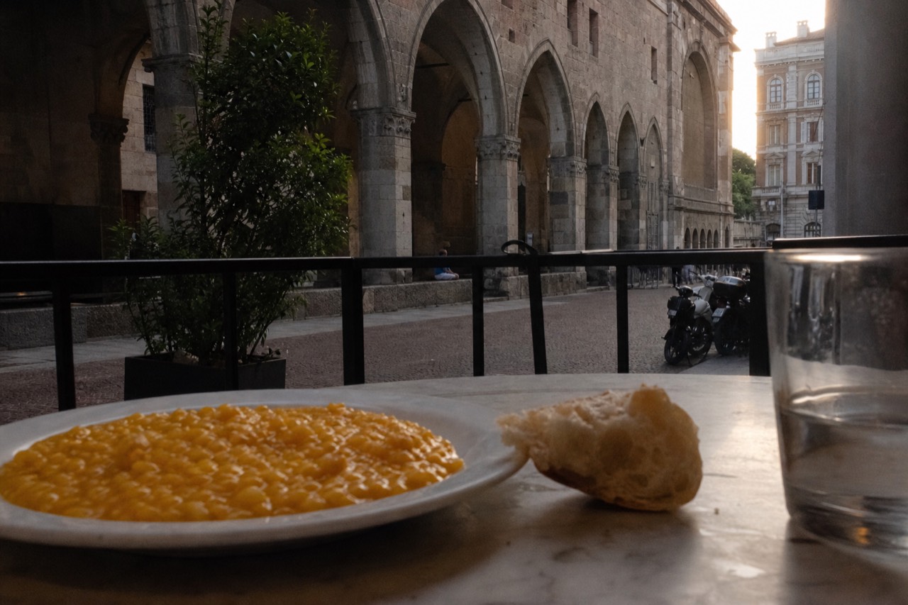 A plate of golden saffron risotto beside a bread roll on a marble table in a Milan restaurant