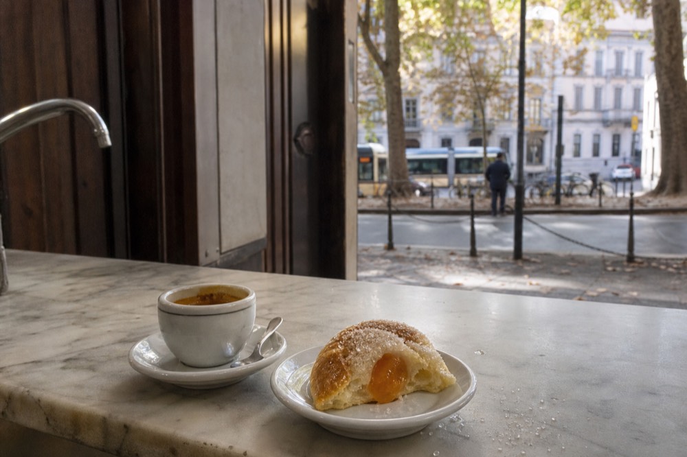 Close view of an espresso cup and a jam-filled brioche on a small saucer at a bar counter