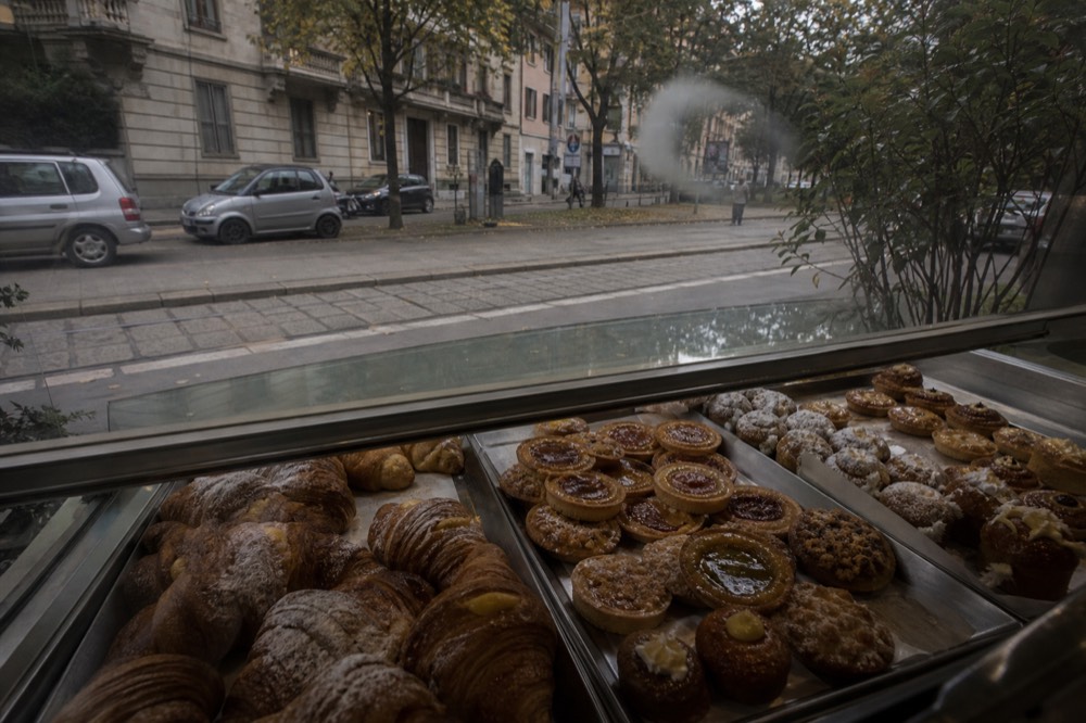 A glass pastry case filled with cornetti, jam tarts and cream-filled brioche in a Milan pastry shop