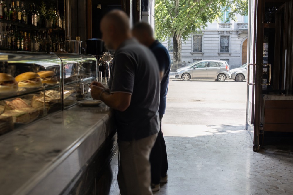 A Milanese bar counter at midday with panini on display and customers standing at the marble