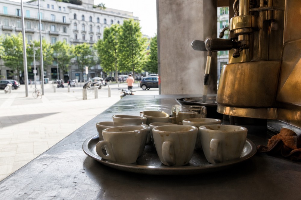A tray of espresso cups lined up on a bar counter beside a brass coffee machine