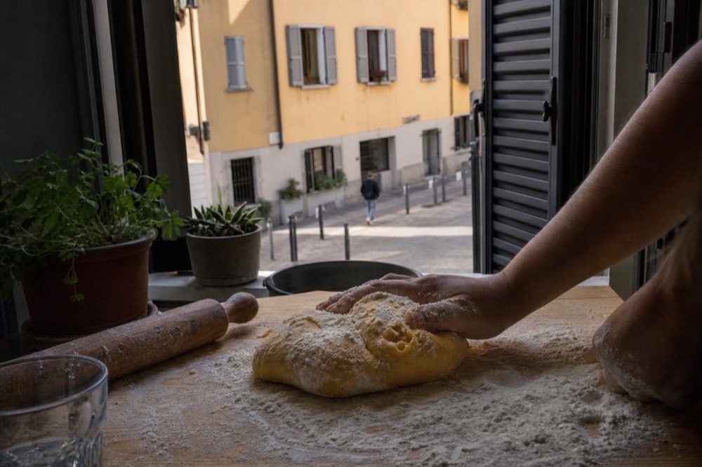 Hands kneading fresh pasta dough on a floured wooden board in a home kitchen