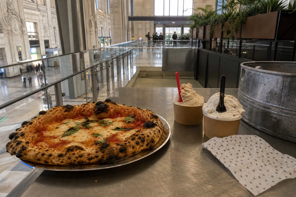 A wood-fired pizza fresh from the oven beside scoops of gelato in cups on a counter