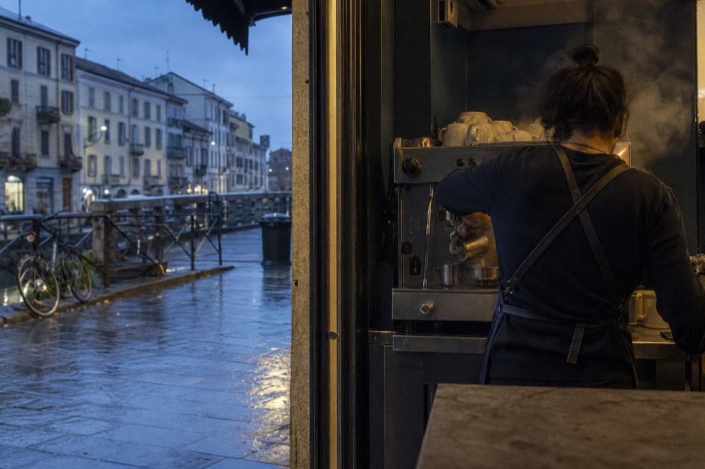 Barista pouring steamed milk behind the counter of a small Milan espresso bar