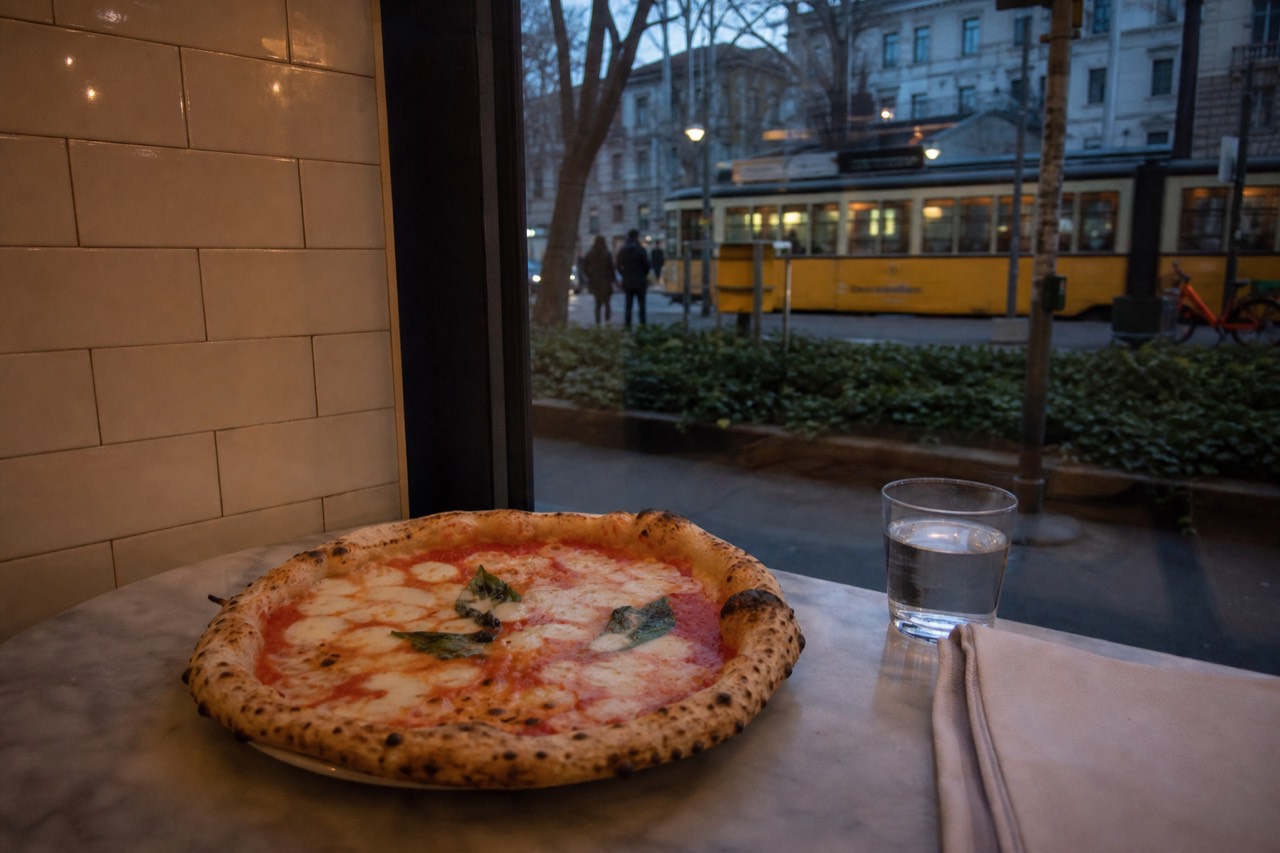 A whole pizza margherita on a marble counter beside a folded napkin and a glass of water