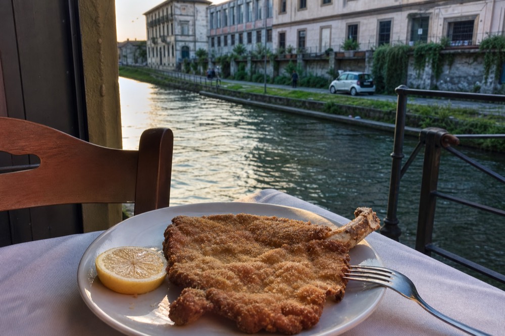 A breaded veal cutlet with the bone resting on a white plate in a Milan trattoria