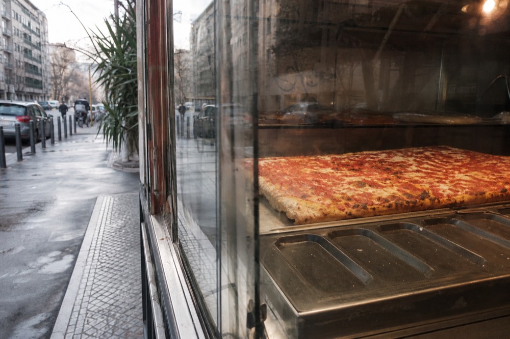 Thick rectangular slab pizza cooling in a bakery display case in Milan
