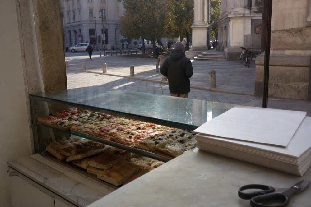 Counter of a Milan bakery with sliced pizza and focaccia trays behind glass