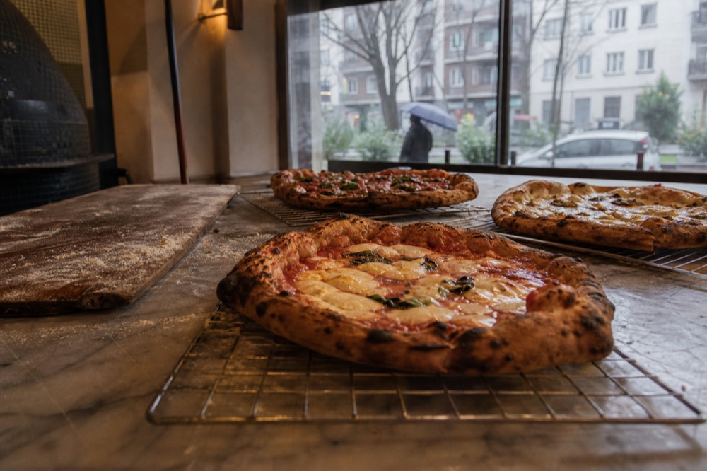 Wood and marble interior of a Milan pizzeria with round pizzas on a counter