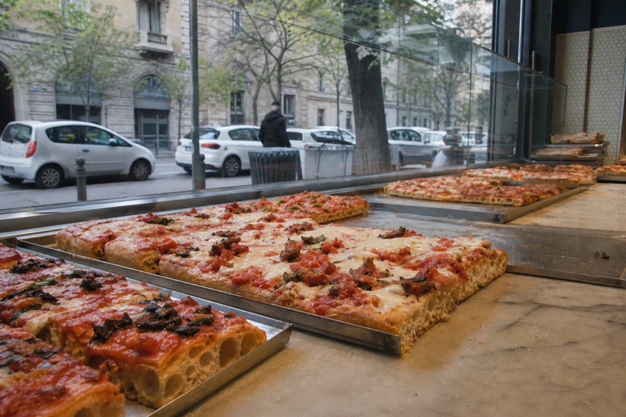 Slabs of thick-crust pizza al trancio displayed on a marble counter in a Milan bakery