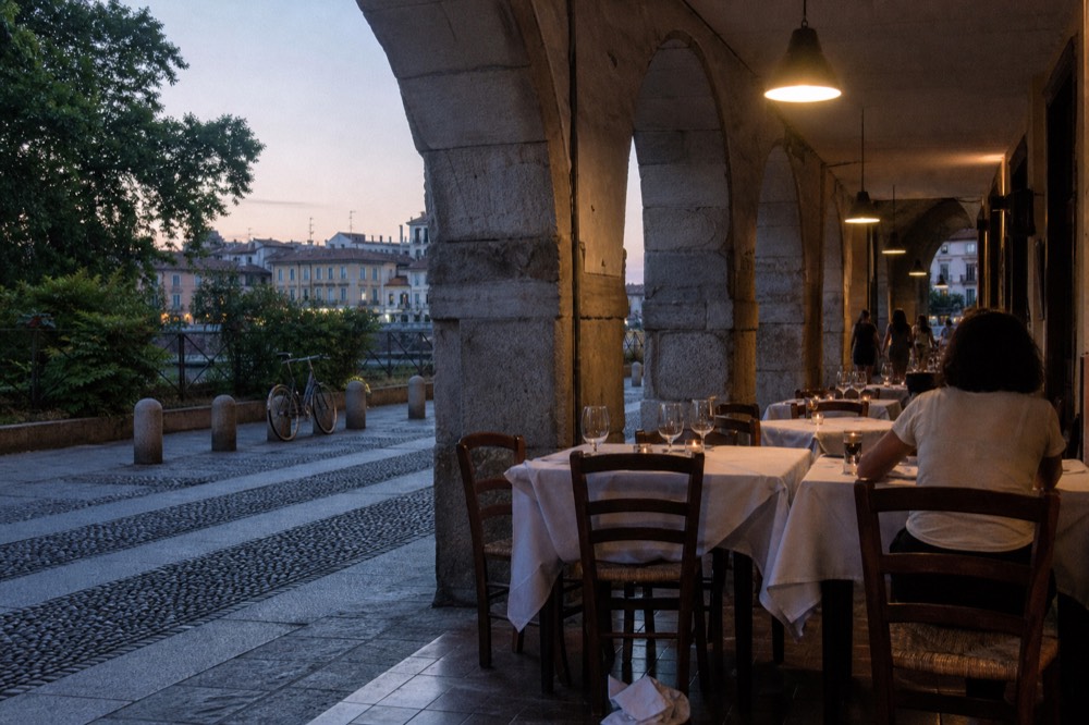 A Milanese dining room at dusk with white tablecloths, wine glasses and soft pendant lights