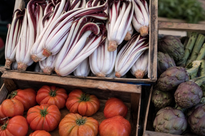 Fresh produce stacked at a Milan market stall with a laid home table beyond
