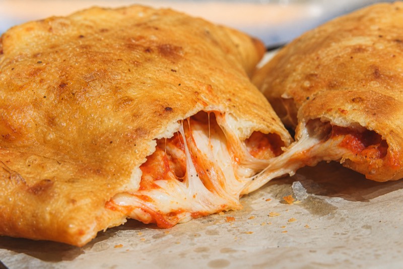 A fried panzerotto torn open in its paper on a steel counter at a Milan street-food stop