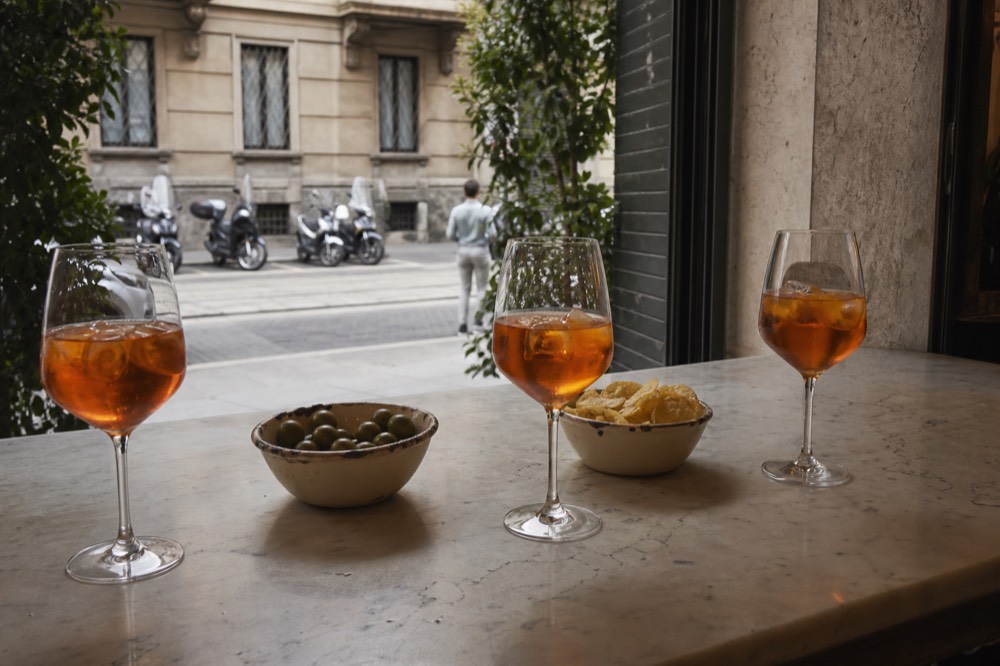 Orange spritz cocktails in wine glasses on a marble bar top with bowls of olives and chips