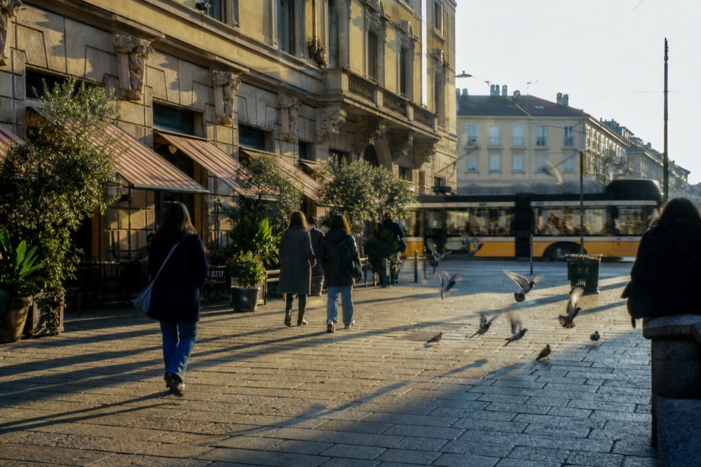 Milan street in late afternoon light with people walking past cafe awnings