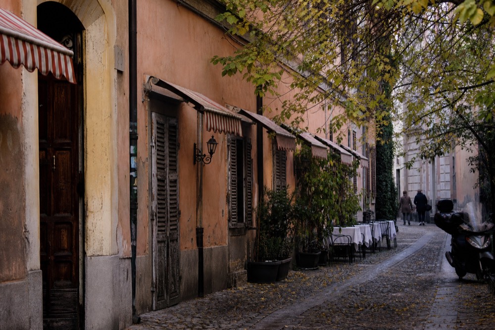 Narrow Brera lane with restaurant awnings and wooden doors in late afternoon