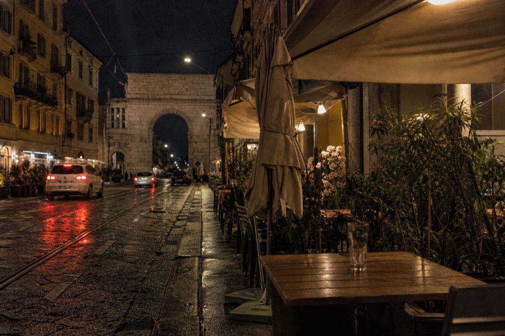 Evening street scene with lit restaurant terraces and people at outdoor tables