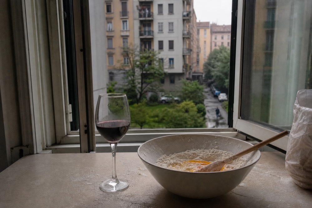 A glass of red wine beside a bowl of flour and eggs on a kitchen counter