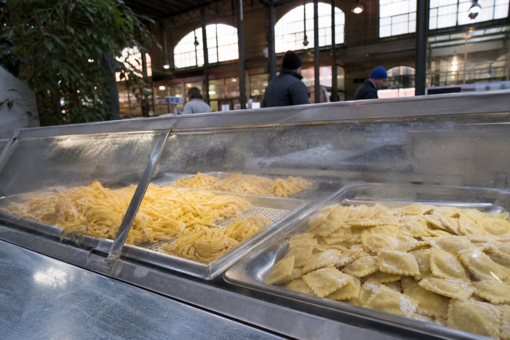 Fresh pasta displayed on a chilled counter with handwritten price labels in an Italian food hall