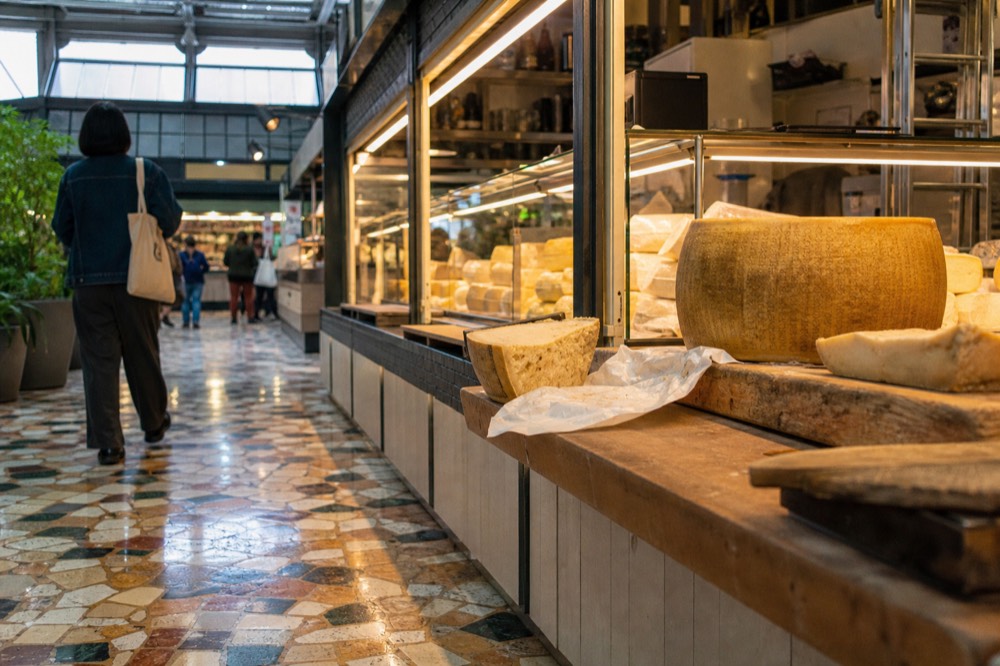 A cheese counter with wheels and wedges of aged cheese on wooden boards under display lighting