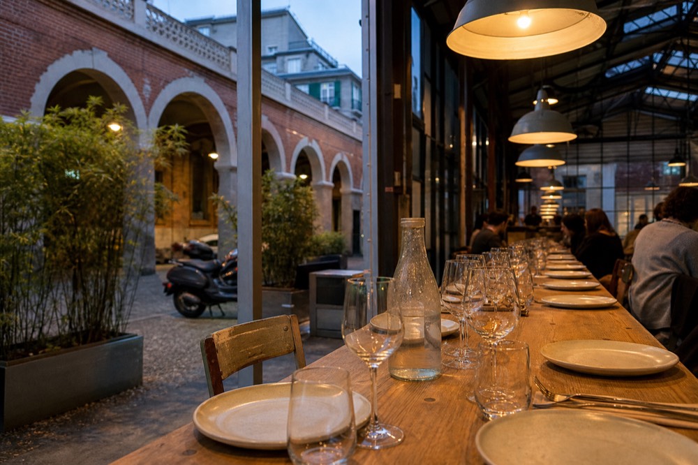 A long wooden dining table set with plates and wine glasses beneath warm ceiling lights