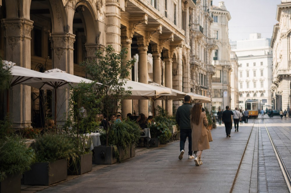 A pedestrian shopping street with restaurant terraces and arcade facades in central Milan