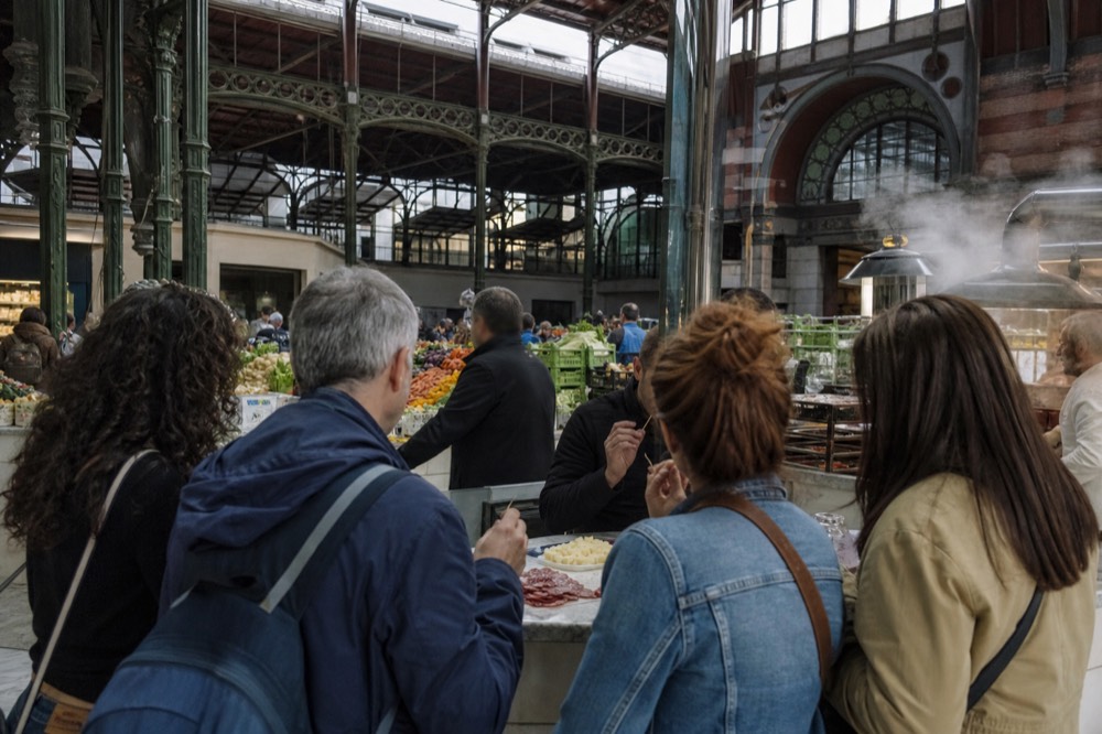 A small group of people tasting food at a market counter with a guide