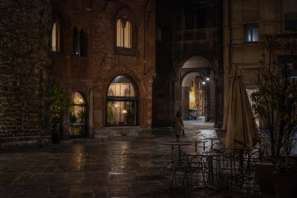 A Milan street at dusk with lit restaurant windows and stone arcades