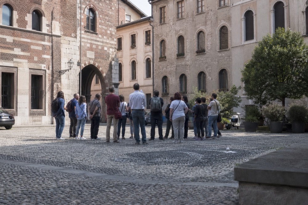 Crowd of walkers gathered around a tour guide in a Milan piazza