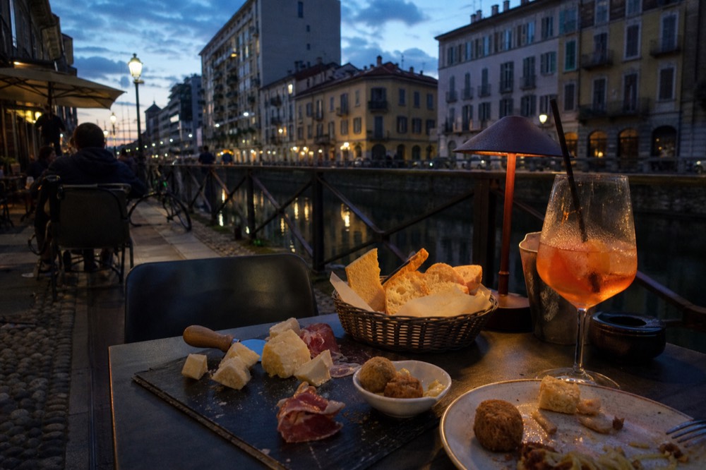 Aperitivo buffet table with bread, cheeses and snacks beside a glass of spritz